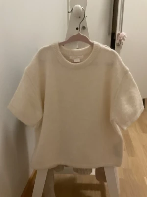 Vit stickad tröja Gina Tricot young - Mysig vit stickad tröja från Gina Tricot i storlek 146/152. Tröjan har korta ärmar och en rund halsringning med ribbad kant. Perfekt för lager på lager och enkel att matcha med olika stilar.