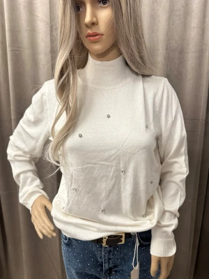 Vit polotröja med pärldetaljer - Snygg vit polotröja med lång ärm och ribbade muddar. Tröjan är dekorerad med små pärlliknande detaljer framtill som ger en extra touch. Perfekt till jeans eller kjol för en clean och trendig look.