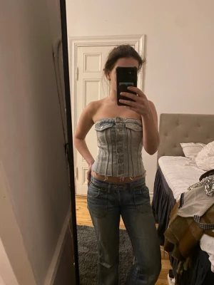 Ljusblå korsett från Zara - Säljer en snygg ljusblå denim korsett från Zara i storlek XS men skulle även säga att den passar S! Toppen är axelbandslös och har knappar framtill samt rå kant nertill för en cool look. 