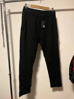 Nya Svarta tapered kostymbyxor från 157 - Helt nya Svarta kostymbyxor från 157 med tapered passform och elastisk midja. Byxorna har fickor fram och bak, och är gjorda i ett mjukt material som ger en clean och stilren look. 