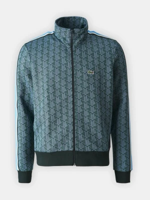 Mönstrad blå zip hoodie från Lacoste - Säljer en blå hoodie från Lacoste med hel dragkedja och hög krage. Tröjan har ett geometriskt mönster, vita och ljusblå ränder längs ärmarna samt den klassiska krokodilloggan på bröstet. Tillverkad i polyester och har ribbade muddar. 