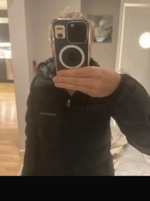 Svart pufferjacka från Peak Performance - Säljer en svart pufferjacka från Peak Performance med hög krage och dragkedja framtill. Jackan är vadderad och har en klassisk, stilren look som passar perfekt när det är kallt ute. Enkel att matcha med olika outfits och riktigt skön att ha på sig.