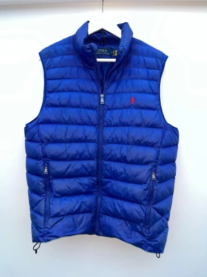 Blå väst Polo Ralph lauren - En fin blå väst från Polo Ralph Lauren. Den passar perfekt som lager på lager och är i mycket gott skick! Enda defekt är att ena midjespännet ej fungerar, men det är inget som syns! Bara att höra av sig om man undrar något👍🏻