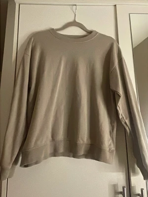 Beige sweatshirt från 157 - En enkel och stilren beige sweatshirt från 157 med rund hals och ribbade muddar vid ärmslut och nederkant. Perfekt för chill dagar och passar till det mesta. Mjuk bomullskänsla och klassisk passform.