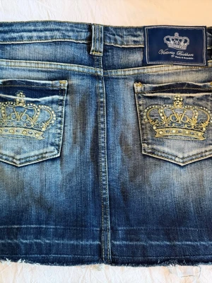 Victoria Beckham jeanskjol  - Säljer denna ursnygga jeanskjol från Victoria Beckham med cool tvätt! Kjolen har två bakfickor med ett komplett guldglittrande kronbroderi och pärldetaljer. Kjolen är som gott som ny💕Inga defekter finns! Hör av dig vid minsta fundering!💕✨