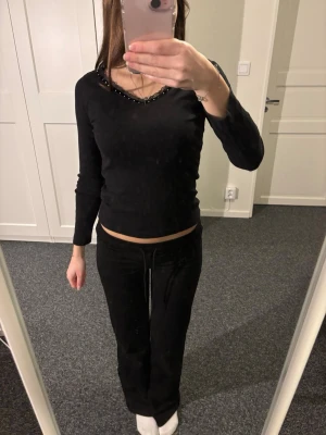 Svart långärmad topp från H&M Young - Svart långärmad topp från H&M Young i storlek 152. Toppen har en v-ringad hals med dekorativa pärlor längs kanten.