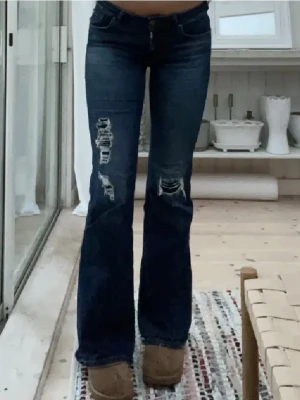 Mörkblå bootcut jeans från ONLY - Säljer ett par mörkblå jeans med bootcut passform och snygga slitningar på båda benen, från ONLY. Dem är klippta längst ner och är lite långa på mig som är 163. De är i storleken 28/34 men då lite kortare eftersom jag har klippt dem lite!💓