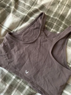 Lila sporttopp från SOC - Säljer en lila sporttopp från SOC i storlek L. Toppen har en enkel, croppad design med breda axelband och rund halsringning. Tillverkad i ett stretchigt syntetmaterial som andas, perfekt för träning. Diskret logga framtill och mesh på insidan för extra ventilation.