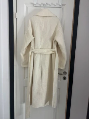 Vit lång kappa från Stockh LM  - Jättefin kappa som är använd 2-3 gånger. Den kommer tyvärr ej till användning, därav säljer jag den. Normal i storleken och jättefin passform. Har tyvärr ingen bild på då jag använt den så sällan. Inga skavanker eller något slitage alls. 🩷  jaden är i boucle, 55% polyester, 30% ull och 15% viskos 😇 Normalpris: 2 999kr