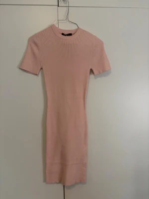 Ribbad ljusrosa klänning Gina Tricot - Säljer en ribbad stickad klänning från Gina Tricot i ljusrosafärg. Modellen är kort med rund hals och korta ärmar. Materialet är mjukt och stretchigt, perfekt för dig som gillar enkel och stilren design. Passformen är slim och klänningen är i storlek XS.