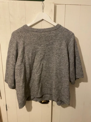 Grå stickad tröja från 157 - Mysig grå stickad tröja från 157 i storlek S. Tröjan har trekvarts ärmar och en rundad hals med ribbad kant. Perfekt för lager-på-lager och chill dagar. Enkel och stilren design som funkar till många olika outfits.