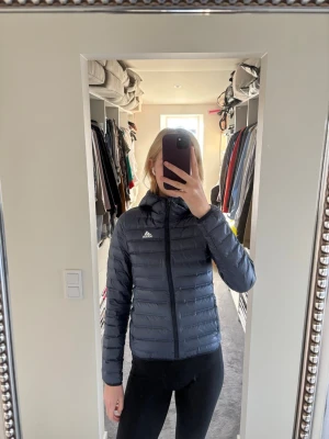 Mörkblå dunjacka från Adidas - Säljer en mörkblå dunjacka från Adidas med luva och dragkedja framtill. Säljer på grund av att den börjar bli för liten/tajt. Funkar både till vardags och till lättare träning.