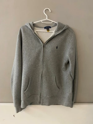 Grå polo Ralph Lauren zip-hoodie - Använd fåtal gånger. Fri frakt!Öppen för frågor! Pris kan diskuteras!  Polo Ralph Lauren Huvtröja Grå Zip-up Dragkedja Logotyp Broderad logga Känguruficka Långärmad Ribbstickade muddar Ribbstickad nederkant Mjuk Bekväm Kvalitet Bomullsblandning Casual Sportig Preppy Klassisk Stilren Vardaglig Mode Herr Dam Unisex Vintage Andrahand Begagnad Ny Oanvänd Barn Vinter vår sommar höst