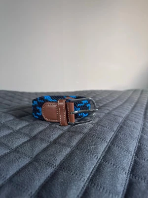 Blå svart flätat bälte - Tja det är helt nytt från Bältgallerian. Det är 105cm långt och 3,5cm brett. Det är i ett elastisk material som passar större storlekar.