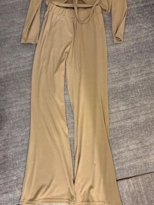 Beige sett  - Säljer mitt sett som är byxor med breda ben och elastisk midja. Samt en topp som har en snörning och är justerbar. Detta sett är gjort i ett mjukt, ribbat material som känns skönt mot huden. Köpt i Egypten därav storleken.  Liten i storlek, står att storleken är L (42) men den passar från storlek M-L.