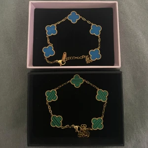Blått och grönt armband med klöver - Två snygga armband med klöverformade länkar i blått och grönt, båda med guldfärgade kedjor. Det blå armbandet har släta länkar medan det gröna har ett randigt mönster. Perfekt för dig som vill ha något unikt och färgglatt på handleden. Båda armbanden 200 kr ett armband 100 kr.