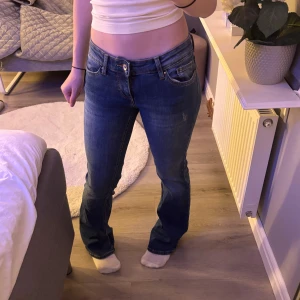 Blå bootcut jeans  -  blå jeans med femficksdesign och låg midja. Modellen har bootcut-ben. 