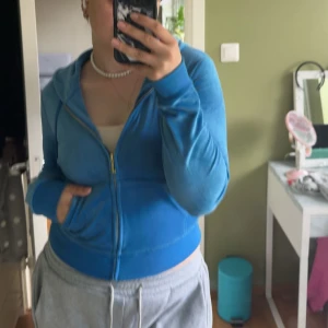 Blå juicy couture hoodie med dragkedja - Säljer en blå juicy couture hoodie med huva och dragkedja framtill. Tröjan har långa ärmar, fickor på sidorna och en skön, avslappnad passform. Perfekt för chill dagar eller när du vill ha något bekvämt och snyggt.