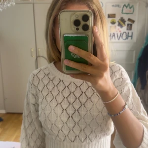 Vit stickad tröja med hålmönster - Säljer en superfin vit stickad tröja med snyggt hålmönster i diamantform. Tröjan har rund halsringning, långa ärmar och bred ribbad mudd i midjan som ger en schysst passform. Perfekt att styla med jeans eller kjol för en fräsch look.