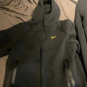 Svarta Nike nocta hoddie och mjukisbyxor med gul logga - Svarta mjukisbyxor från Nike med en gul swoosh-logga på benet. Byxorna har en sportig look och är tillverkade i mjukt material som passar perfekt för chill eller träning. Klassisk passform med resår i midjan och raka ben. Tröjan är xl med passar mer en L 