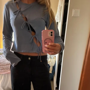 Blå croppad topp med knyt från Monki - Trendig blå croppad långärmad topp från Monki med cool sned öppning framtill och flera knytband. Toppens material är mjuk bomull och den har en relaxed fit som ger en chill vibe. Perfekt för dig som vill sticka ut med snygga detaljer.