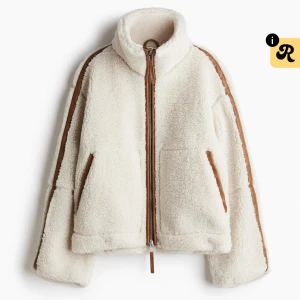 Pilejacka från HM - Supermjuk teddyjacka i beige med bruna detaljer längs dragkedja, fickor och ärmar. Jackan har hög krage, två stora fickor och oversized passform. Perfekt för kalla dagar när du vill vara både varm och snygg. Den virala teddyjackan slut överallt!!!!