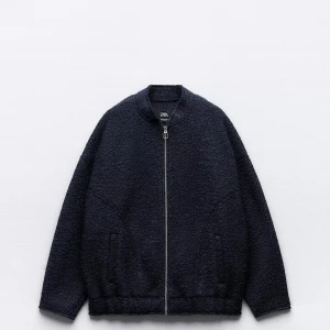 Svart teddyjacka från Zara - Mysig mörkblå teddyjacka från Zara med oversized passform och grov dragkedja framtill. Jackan har rundad krage, två fickor och är tillverkad i ett fluffigt teddy-material som ger en cool och avslappnad vibe. Perfekt att slänga på sig över en hoodie eller stickad tröja.