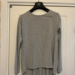 Grå långärmad tröja - Enkel och stilren grå tröja med lång ärm och rund hals. Tröjan har en lös passform och ett rynkat parti baktill som ger en avslappnad look. Perfekt för dig som gillar basic och comfy vibes.