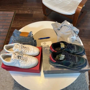 Valentino sneakers, vita och camo - Två par Valentino sneakers: ett par helvita med rund tå och snörning, samt ett par med camouflage-mönster i grönt, svart och rött med svarta snören och röd häl. Båda paren har platt sula och klassisk sneakerform. Perfekta för dig som gillar streetstyle och exklusiva märken.