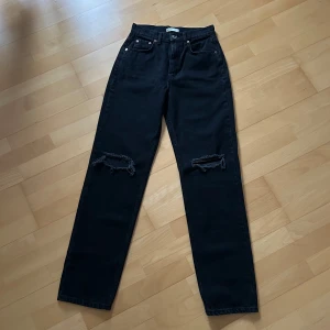 Svarta straight jeans från Gina Tricot - Svarta jeans med raka ben från Gina Tricot. Modellen har hög midja och slitna detaljer vid knäna för en cool look. Klassisk knappgylf. Perfekta för dig som gillar en avslappnad men trendig stil.