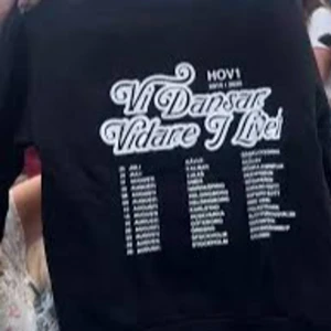 Svart Hov1 hoodie Vi Dansar Vidare - Svart hoodie från Hov1 med stor vit text 'Vi Dansar Vidare I Livet' och turnédatum på ryggen. Perfekt för dig som älskar svensk musik och vill ha en snygg och bekväm tröja med streetkänsla. Klassisk passform och mjukt material. I storlek S