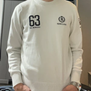 Vit tröja från Henri Lloyd med tryck - Vit långärmad tröja från Henri Lloyd med logga på bröstet samt brittisk flagga på ärmen. Tröjan har ribbade muddar och rund hals. En liten fläck på axeln som jag är övertygad om går bort i tvätten. Tveka inte på o höra av er om ni har fler frågor:)