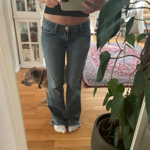 bootcut jeans - Säljer ett par blå Levis jeans med bootcut-modell och låg midja. Jeansen har klassiska fem fickor, slitna och råa kanter nertill för en cool vibe. Materialet är klassisk jeans och passformen är normal. Perfekta för dig som gillar en avslappnad stil. Skriven med AI skriv för fler frågor! Priset är ej diskuterbart❤️❤️ Mått: 37 rätt över Innerbenslängd: 81