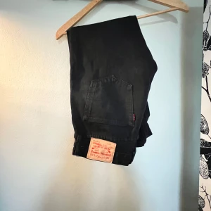 Svarta Levi's 501 jeans - Klassiska svarta Levi's 501 jeans med rak passform och femficksdesign. Jeansen har den ikoniska läderpatchen bak och är tillverkade i slitstarkt bomullsjeans. Perfekta för dig som gillar en tidlös och clean look.