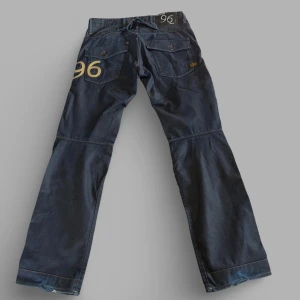 mörkblå jeans från G-Star RAW - Säljer ett par mörkblå jeans från G-Star RAW. Knappar vid gylf. Mycket detaljer. Midja 45 cm. Innerbenslängd 82 cm