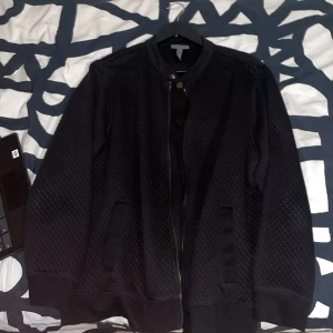 Svart quiltad bomberjacka H&M  - Svart bomberjacka från H&M i storlek XL men den passar i M. Jackan har quiltat mönster, dragkedja framtill och ribbade muddar vid ärmslut och nederkant. Enkel och stilren design med två fickor på sidorna och rund krage med knappdetalj.