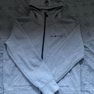 Grå Sailracing Zip - Grå fullzip från Sail Racing i storlek 170 - sitter som Xs. Varsamt använd i väldigt bra skick. Nytt pris: 1400kr. Mitt pris: 129kr