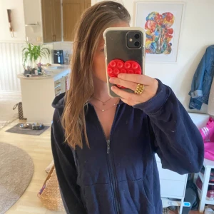 Mörkblå hoodie med dragkedja - Mysig mörkblå hoodie med dragkedja framtill och huva. Tröjan har långa ärmar och en avslappnad passform, perfekt att slänga på sig när det är lite kyligt. Klassisk stil som funkar till det mesta och är superenkel att matcha.