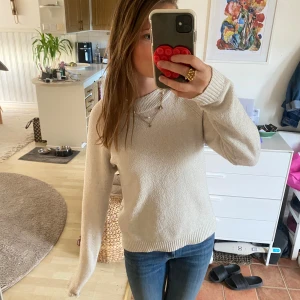 Beige stickad tröja med rund hals - Mysig beige stickad tröja med rund halsringning och ribbade muddar vid ärmslut och nederkant. Perfekt för lager-på-lager och enkel att matcha med jeans eller kjol. Långärmad och i en klassisk, avslappnad passform.