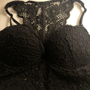 Svart spetsig bh - Säljer en svart spetsig bh med tunna axelband och vackert blommigt spetsmönster. Toppen har vadderade kupor och detaljerad spets både fram och bak, vilket ger en riktigt snygg och feminin look. 