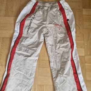 Snygga, pösiga byxor från jaded London! - Sportiga täckbyxor från Jaded London i vitt med röda och svarta detaljer längs sidorna. Kan även användas som trackpants men är tjockare i materialet. Säljer pga ingen användning. Fråga för fler bilder eller mått💕