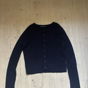 Mörk blå kabelstickad kofta Brandy Melville - Mörkblå kabelstickad kofta från Brandy Melville med rund halsringning och knappar hela vägen framtill. Långärmad och i mjukt material, perfekt för lager på lager. Klassisk och enkel design som funkar till allt.