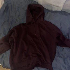 Mörk vinröd hoodie med huva - Säljer en mörk vinröd hoodie med huva och snörning. Tröjan har en relaxed passform och långa ärmar, perfekt för chill dagar. Materialet känns mjukt och skönt mot huden. Enkel design utan synliga loggor eller mönster, passar dig som gillar stilrena plagg.
