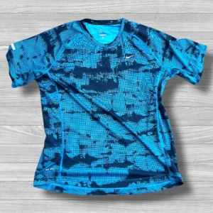 Nike Dri-Fit - Nike Dri-Fit t-shirt i blått med coolt rutigt och abstrakt mönster i mörkblå toner. T-shirten har korta ärmar, rund hals och är gjord i ett lätt, ventilerande syntetmaterial som passar perfekt för träning. Swoosh-logga på bröstet för extra sportig vibe.