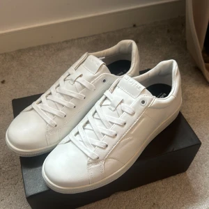 Vita sneakers från Björn Borg - Stilrena vita sneakers från Björn Borg med klassisk design. Skorna har snörning, rund tå och är tillverkade i slätt syntetmaterial med diskret logga på plösen och innersulan. Perfekta för en clean och fräsch look. Aldrig använda!!! Helt nya, nypris 899kr