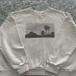 Vit sweatshirt med print från Pull&Bear - Säljer en vit sweatshirt från Pull&Bear i storlek XS. Tröjan har ett svartvitt print med palmer och texten 'Wild as a jungle' och 'Be calm and chill out' på bröstet. Mjuk insida, rund hals och ribbade muddar vid ärmslut och nederkant.