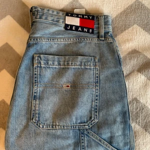 Tommy Jeans ljusblå jeansshorts - Säljer ett par ljusblå jeansshorts från Tommy Jeans med stora bakfickor, synlig logga och coola detaljer som röd söm och uppvikta ben. Klassisk denimkänsla och robust bomullsmaterial. Perfekt för dig som gillar streetwear och avslappnad stil.