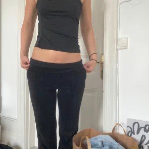 Svarta juicy byxor med fickor i storlek XS - Säljer ett par svarta juicy byxor med raka ben. Byxorna har två stora fickor med knappar bak och mjuk, skön känsla i materialet. Perfekta om du gillar chill och retrovibe. Passar dig som vill ha en loose fit och cool look.