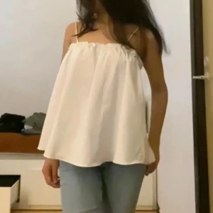 Vit linnetopp - Supersöt vit linnetopp med tunna axelband och rynkad kant upptill. Modellen är lös och flowy, perfekt för varma dagar. Toppen är ärmlös och har en enkel, stilren look som passar till jeans eller kjol.