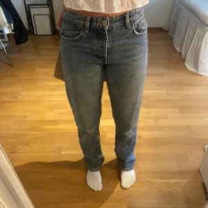 jeans med rak passform - Säljer ett par jeans i blå tvätt med rak passform och hög midja. Jeansen har fem fickor, knappgylf och bälteshällor. Materialet är robust denim i bomull och färgen är en snygg mellanblå ton. Perfekt för dig som gillar tidlös stil.